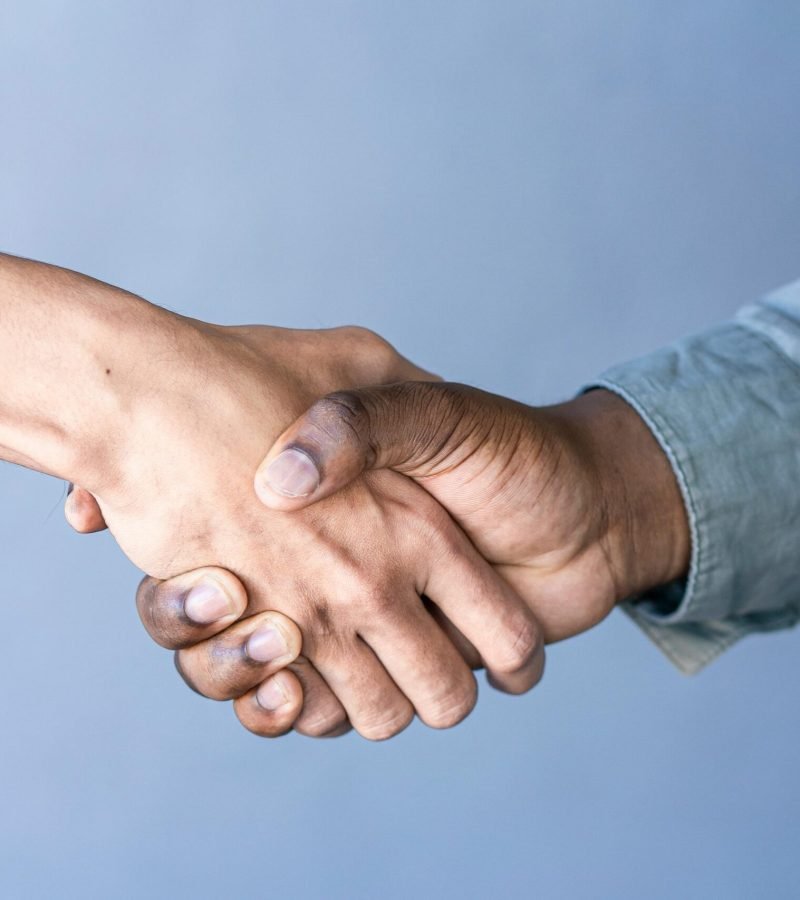 Close-up of a handshake between two people against a blue backdrop.